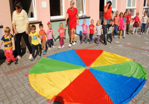 dzieci ustawione w kole tańczą z nauczycielkami na tarasie przedszkolnym wokół kolorowych chust